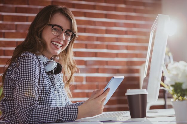 Homme d&#39;affaires hipster souriant à l&#39;aide de la tablette à son bureau dans le bureau