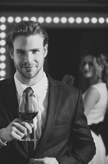 Homme d'affaires ou homme souriant avec barbe et coiffure en tenue formelle avec cravate rouge tenir un verre de vin près d'une femme dans une réunion de miroir et se détendre bar et restaurant sommelier dégustation et dégustation