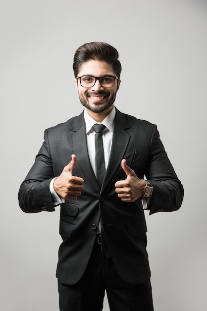 Photo homme d'affaires indien barbu célébrant le succès avec les pouces vers le haut ou levant le poing en se tenant isolé sur fond noir