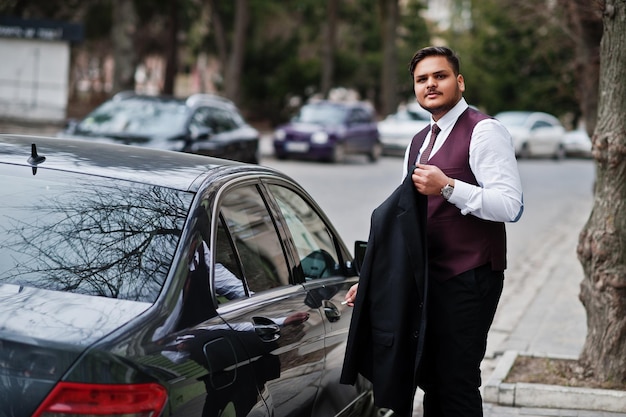 Homme d'affaires indien élégant en tenue de soirée debout contre une voiture d'affaires noire dans la rue de la ville Ouvrir la porte de la voiture par clé