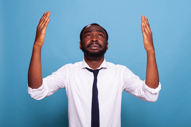 Homme d'affaires inquiet priant en levant les mains levées vers le ciel agissant humblement. Employé émotif en chemise blanche avec cravate noire demandant pardon.