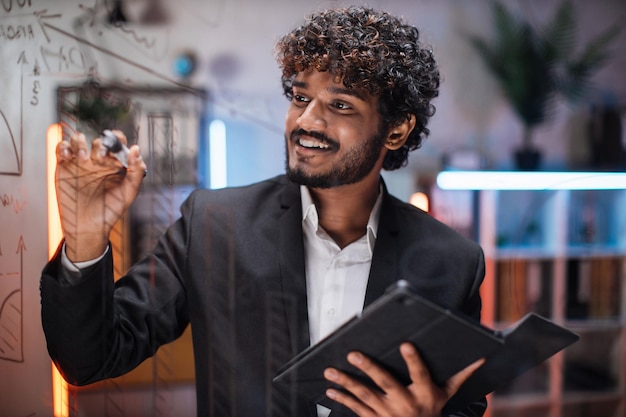 Homme d'affaires intelligent ciblé dessinant des graphiques sur un tableau de présentation en verre