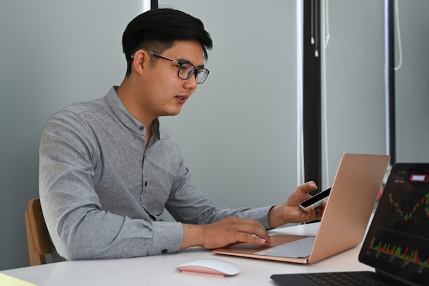 Homme d'affaires intelligent utilisant un téléphone portable et travaillant avec un ordinateur portable sur son lieu de travail.