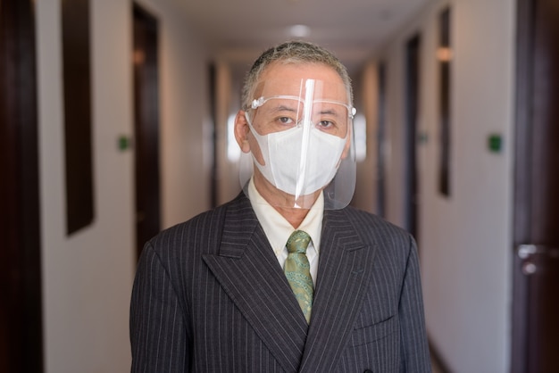 Homme d'affaires japonais mature avec masque et masque facial dans le couloir