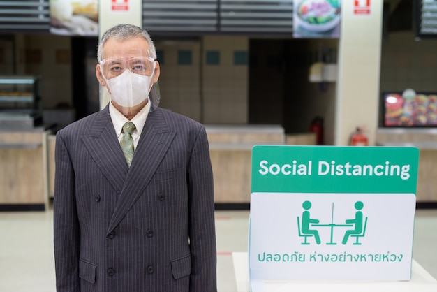 Homme d'affaires japonais mature avec masque et masque facial distance sociale à l'aire de restauration