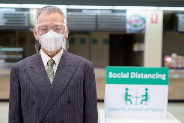 Homme d'affaires japonais mature avec masque et masque facial distance sociale à l'aire de restauration