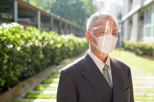 Homme d'affaires japonais mature avec masque et masque facial pensant au parc