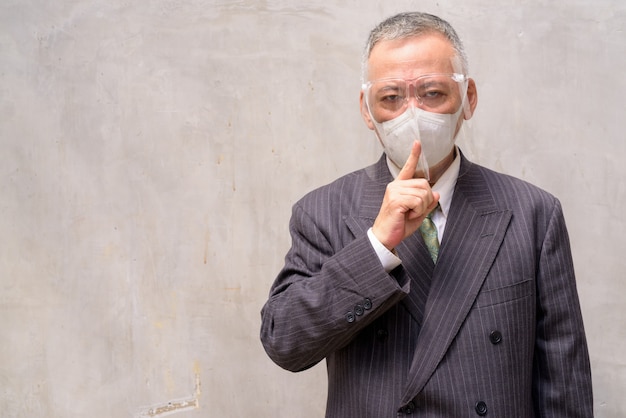 Homme d'affaires japonais mature portant masque et masque facial avec le doigt sur les lèvres