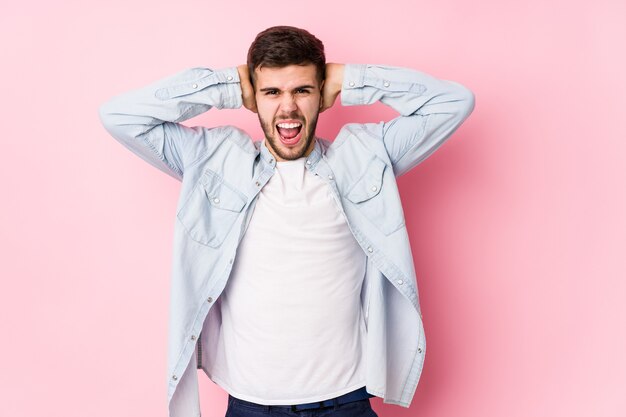 Homme d'affaires jeune caucasien posant dans un blanc couvrant les oreilles avec les mains en essayant de ne pas entendre un son trop fort.