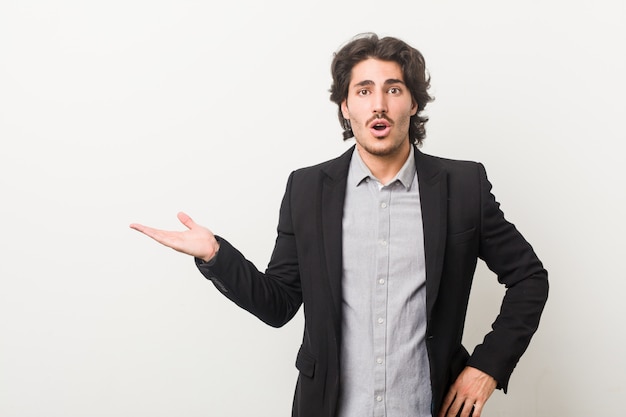 Homme d'affaires jeune contre un mur blanc impressionné tenant copie espace sur palm.