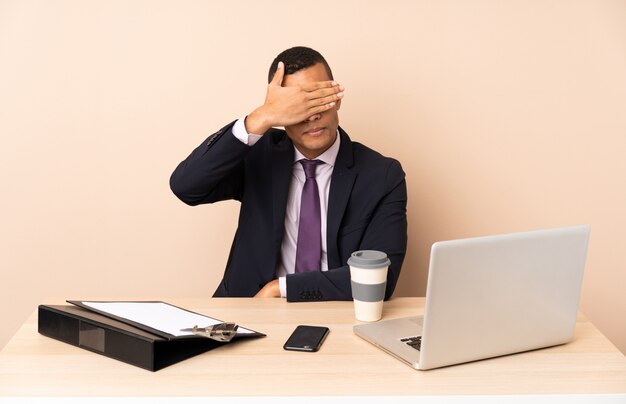 Homme d'affaires jeune dans son bureau avec un ordinateur portable et d'autres documents couvrant les yeux par les mains. Je ne veux pas voir quelque chose