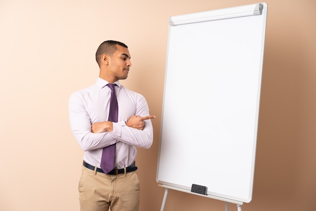 Homme d'affaires jeune sur mur isolé donnant une présentation sur tableau blanc et en le pointant