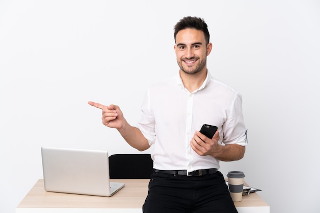 Homme d'affaires jeune avec un téléphone portable dans un lieu de travail pointant le doigt sur le côté