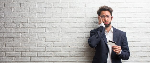 Homme d&#39;affaires jeune vêtu d&#39;un costume contre un mur de briques blanches inquiet et accablé