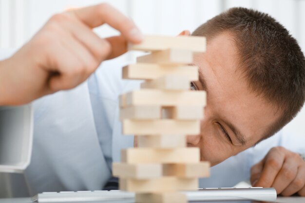 Homme d'affaires joue dans la stratégie à la main en réorganisant les blocs de bois impliqués pendant la pause au travail dans le bureau assis table de jeu pile plaisir joie passe-temps concept