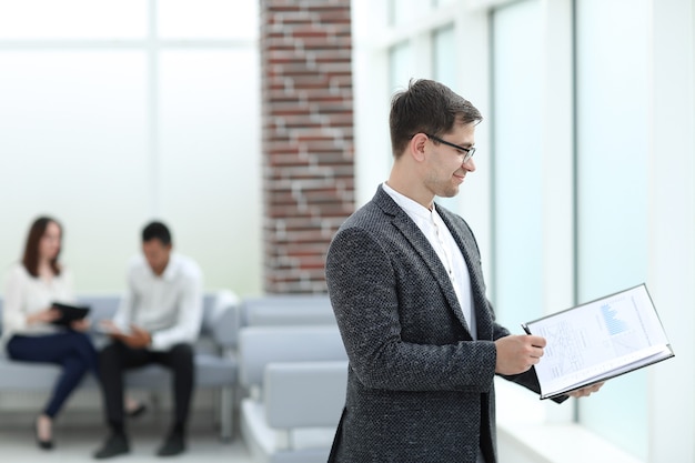 Homme d'affaires lisant des documents commerciaux debout dans le hall du bureau