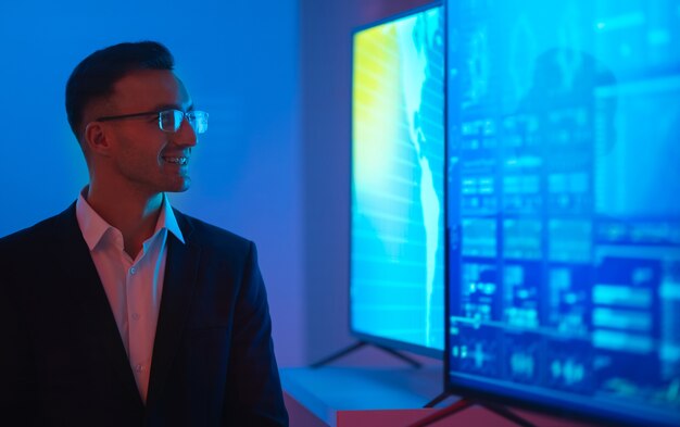 L'homme d'affaires à lunettes debout près de grands écrans avec des graphiques