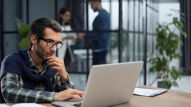 Homme d'affaires à lunettes et vêtements décontractés travaillant sur ordinateur portable dans un bureau moderne