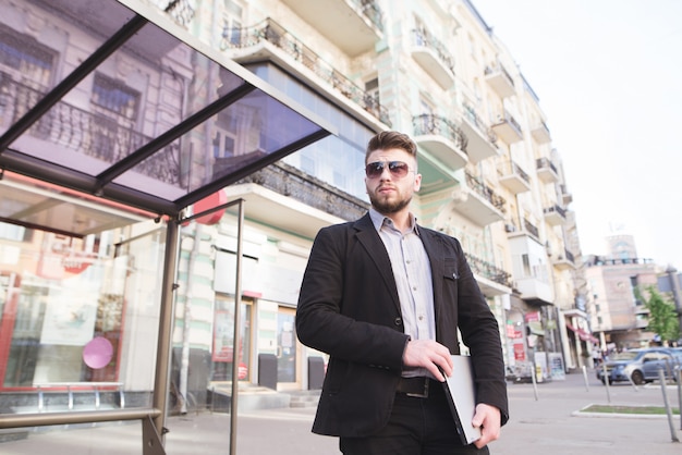 Un homme d'affaires malheureux debout avec un ordinateur portable dans ses mains sur fond d'architecture.