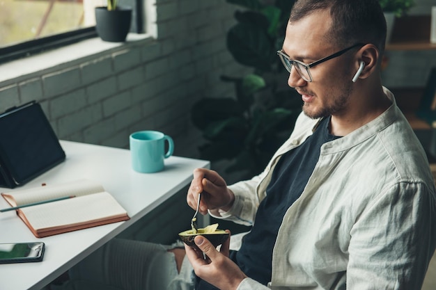 Homme d'affaires mangeant un avocat avec une cuillère pendant la pause de travail communiquant par casque sans fil