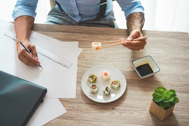 Homme d'affaires manger des sushis à l'heure du déjeuner tout en travaillant au nouveau projet