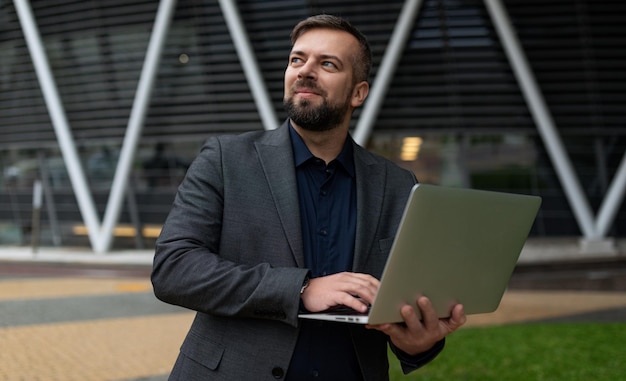 Homme d'affaires masculin adulte avec un ordinateur portable sur le fond d'un immeuble de bureaux économique