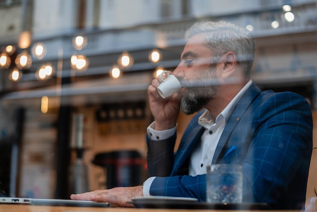 Un homme d'affaires mature assis à son bureau dans le café du bureau ou du restaurant et buvant un café