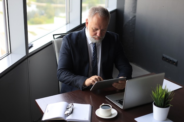 Homme d'affaires mature en costume complet utilisant une tablette numérique alors qu'il était assis au bureau.