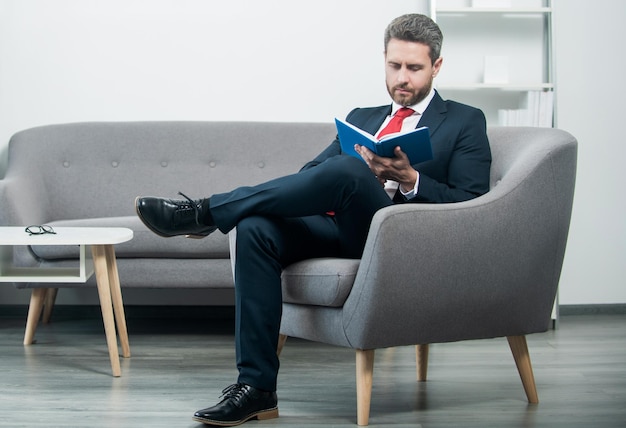 Homme d'affaires mature en costume s'asseoir au bureau lire un livre