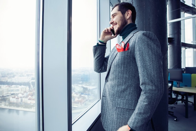 Homme d'affaires mature debout à l'intérieur d'un immeuble de bureaux et utilisant un téléphone portable. Homme debout près de la fenêtre et parlant au téléphone mobile.