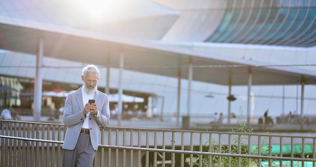 Homme d'affaires mature plus âgé utilisant un smartphone debout dans la ville à l'extérieur
