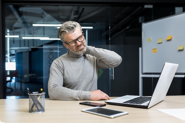 Homme d'affaires mature senior travaillant à l'intérieur d'un immeuble de bureaux homme aux cheveux gris malade et fatigué massant