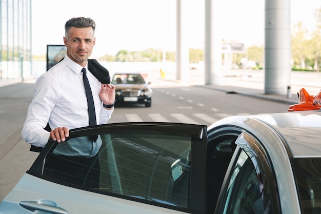 Homme d'affaires mature souriant, monter en taxi à l'extérieur