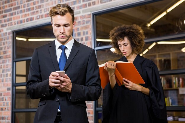 Homme d'affaires, messagerie texte sur smartphone et avocat, lecture de livre de loi