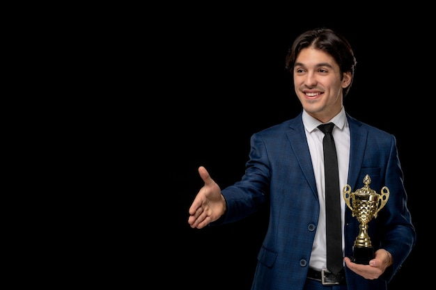 Homme d'affaires mignon mec souriant en costume bleu foncé avec la cravate donnant la poignée de main avec le trophée