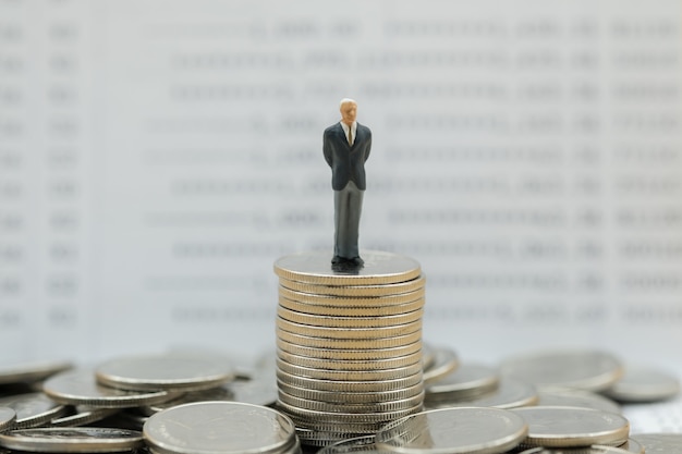 Homme d&#39;affaires miniature figure sur pile de pièces avec livret bancaire