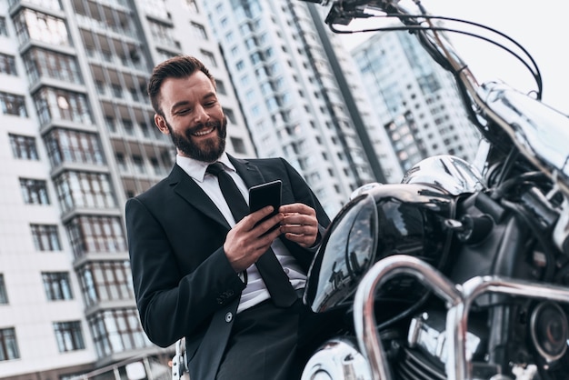 Homme d'affaires moderne. Beau jeune homme en costume complet à l'aide de son téléphone intelligent et souriant