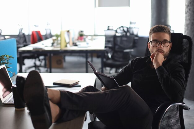 Homme d'affaires moderne concentré travaillant et prenant des notes dans son bureau moderne, les jambes sur le bureau.