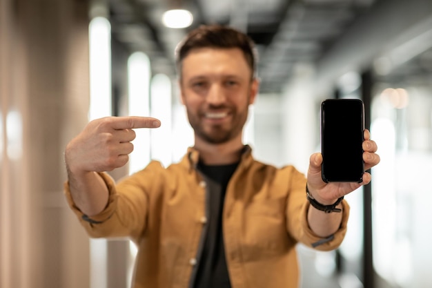 Homme d'affaires montrant un écran vide de smartphone debout dans un bureau moderne