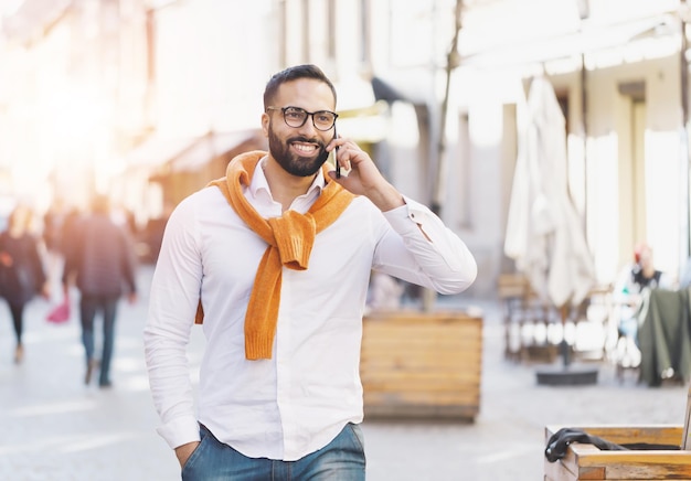 Homme d'affaires multiculturel barbu marchant dans la rue tout en parlant sur le smartphone