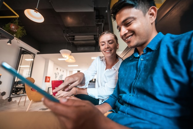 Homme d'affaires multiethnique avec une collègue travaillant ensemble sur une tablette dans la zone de détente du bureau de démarrage moderne. Photo de haute qualité