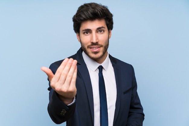 Homme d&#39;affaires sur mur bleu isolé invitant à venir avec la main. Heureux que tu sois venu