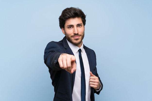 Homme d&#39;affaires sur un mur bleu isolé pointe le doigt vers vous avec une expression confiante