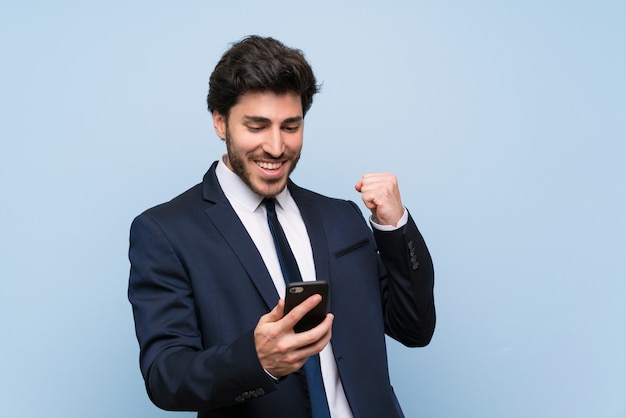 Homme d&#39;affaires sur un mur bleu isolé avec téléphone en position de victoire