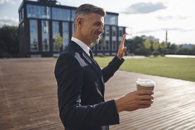 Homme d'affaires mûr confiant tenant une tasse de café tout en se tenant près d'un immeuble de bureaux