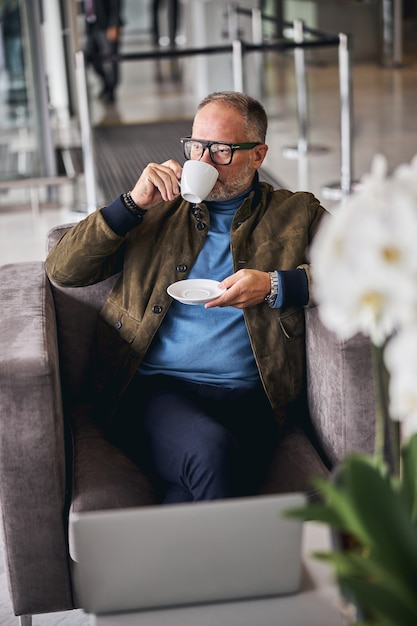 Homme d'affaires mûr réfléchi dans des lunettes buvant du café