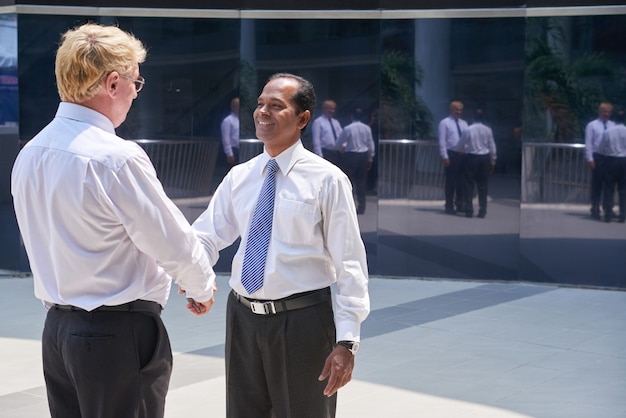 Photo homme d'affaires mûr souriant saluant son partenaire commercial international et lui serrant la main