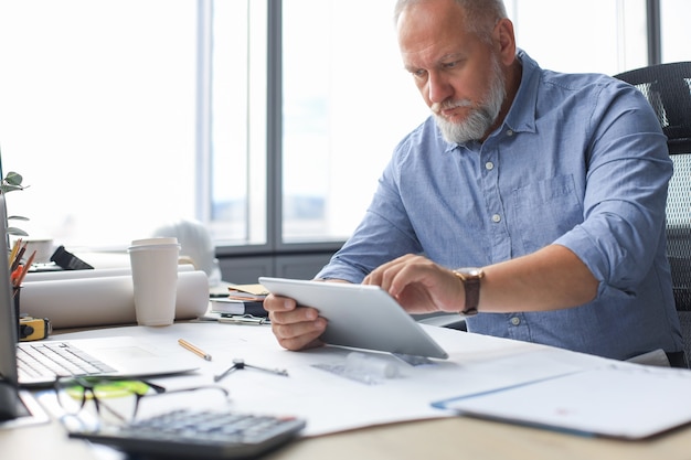 Homme d'affaires mûr travaillant à l'aide d'une tablette numérique alors qu'il était assis dans le bureau moderne.