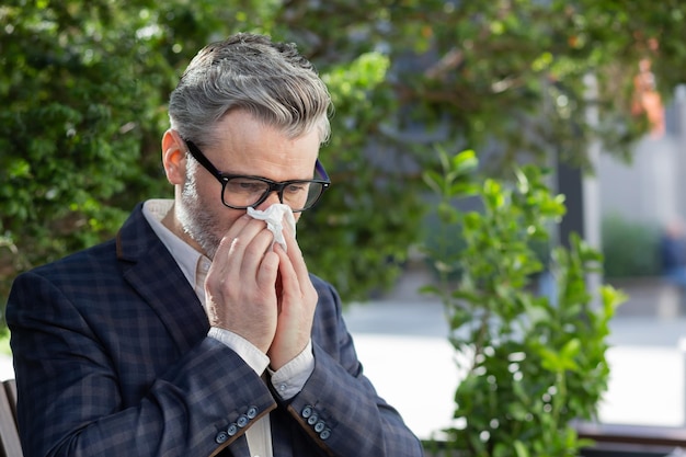 Homme d'affaires mûr travaillant à l'extérieur avec un ordinateur portable homme âgé éternuant d'allergies assis sur le parc