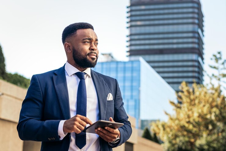 Photo un homme d'affaires noir en costume qui utilise une tablette dehors. il a l'air concentré.
